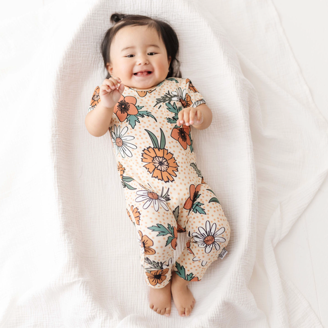 Baby wearing a floral onesie on a white blanket