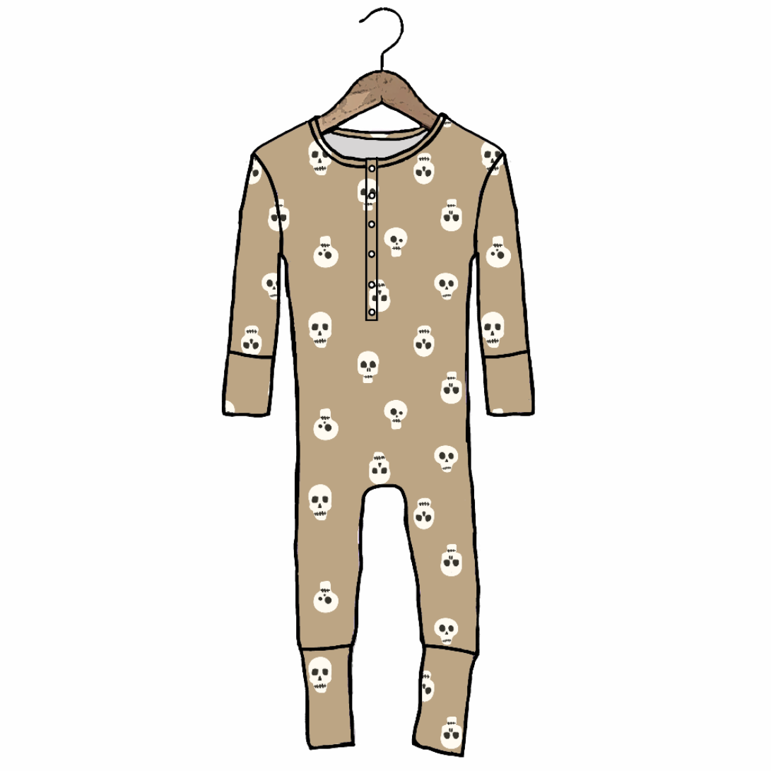 A long-sleeve baby jumpsuit in tan with a repeating white skull and crossbones pattern, hanging on a wooden hanger against a plain white background.