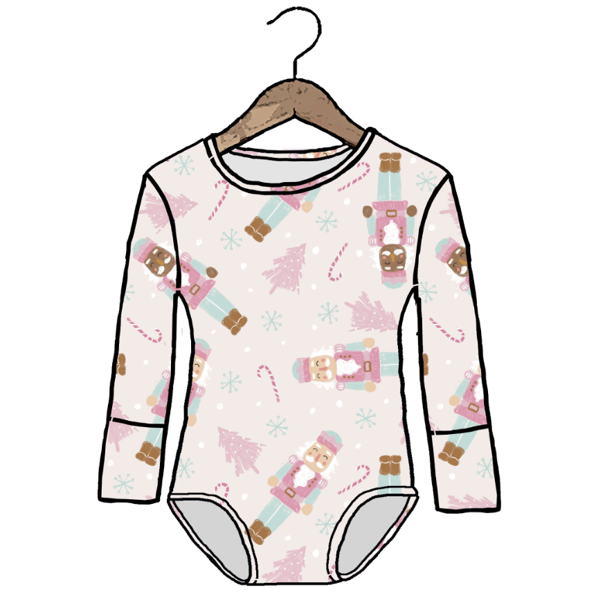 A long-sleeve baby bodysuit with a festive holiday print of nutcrackers, Christmas trees, and candy canes on a light pink background, shown hanging on a wooden hanger against a white background.