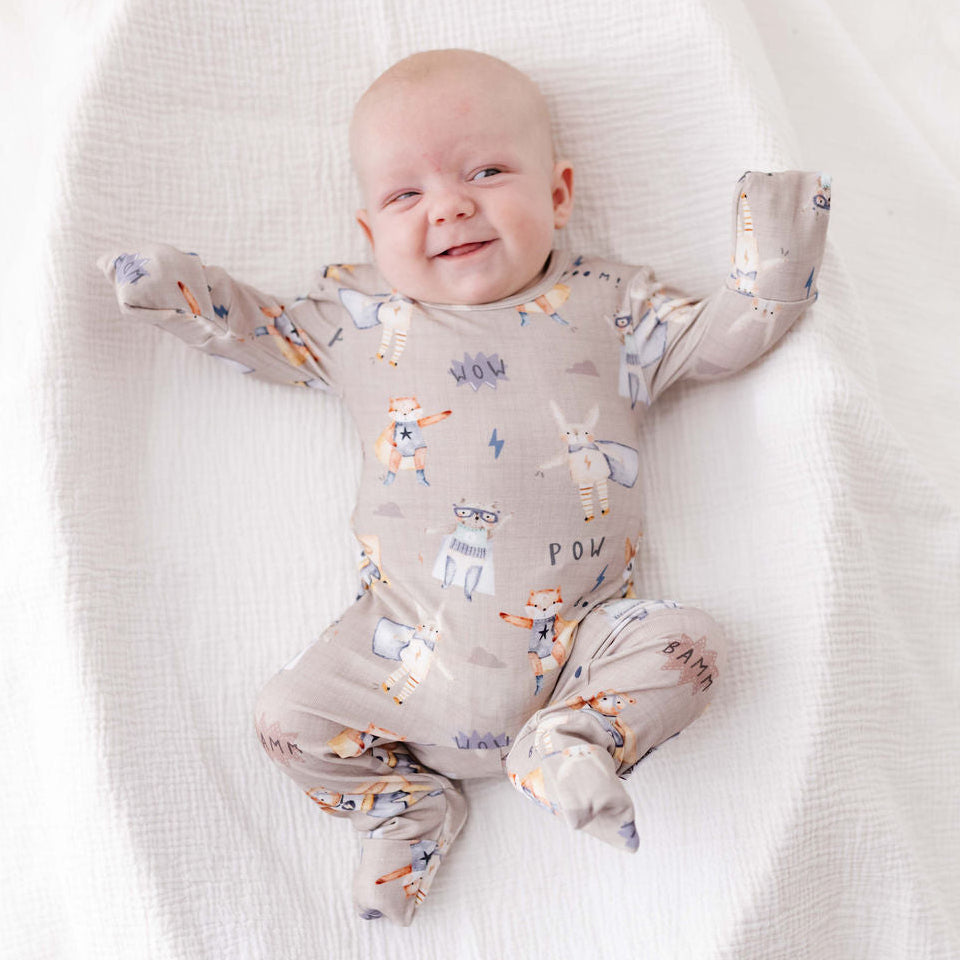 Baby lying on a white blanket wearing a patterned onesie.