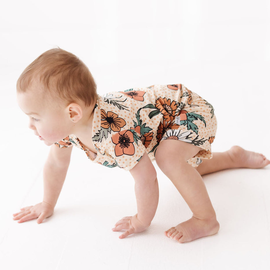 Baby crawling on a white surface wearing a floral romper.
