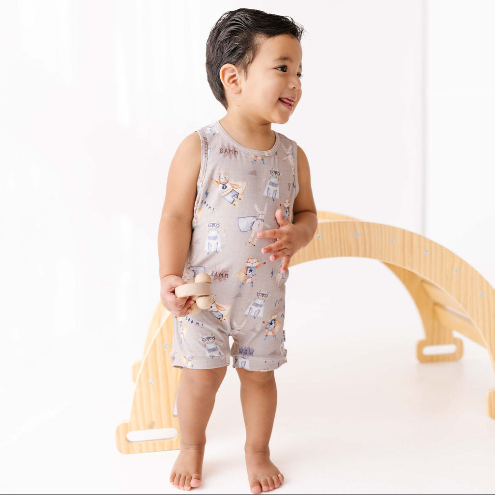 Child wearing a sleeveless romper with animal prints, standing next to a wooden toy.