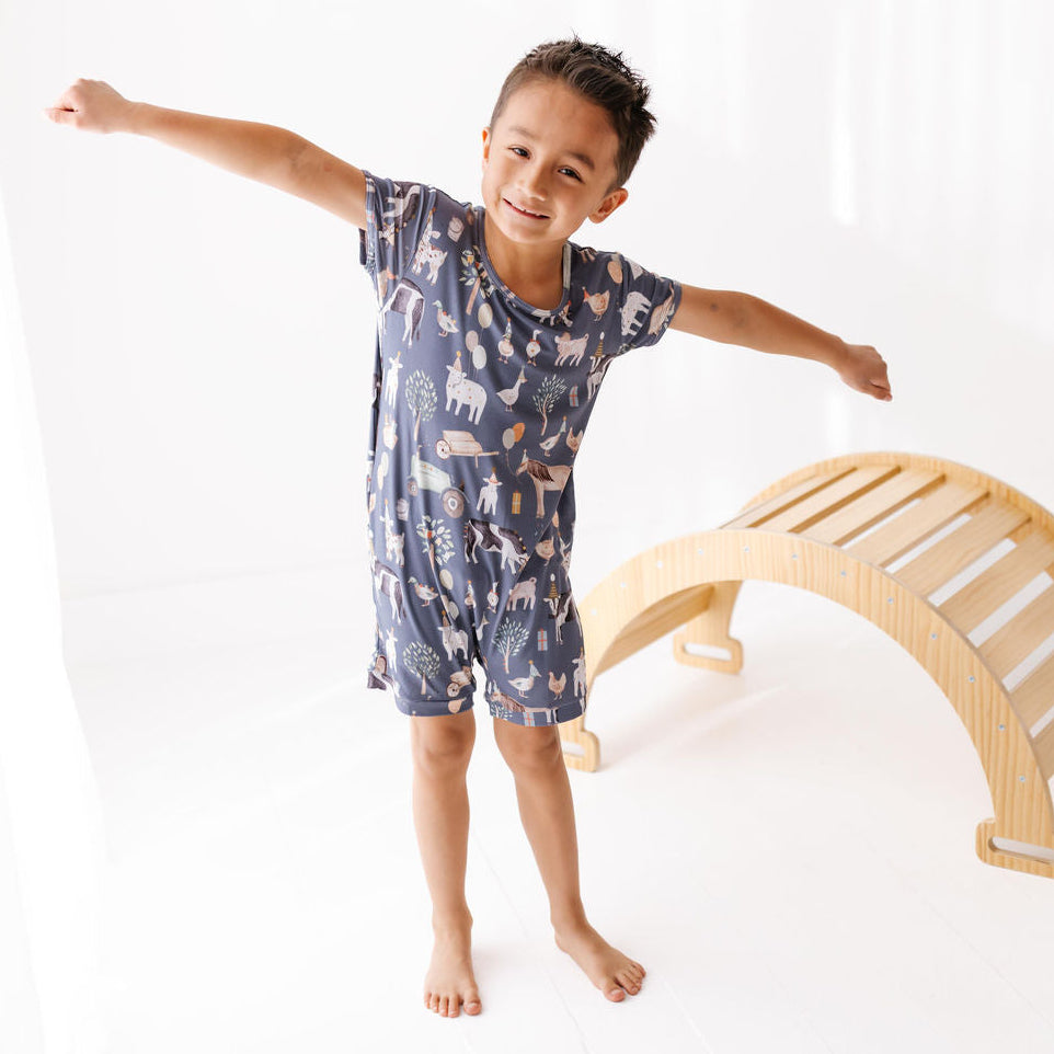 Child wearing a blue pajama set with animal pattern, standing next to a wooden climbing toy on a white background