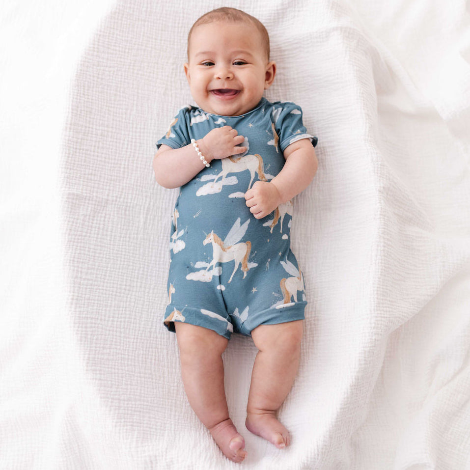 Baby wearing a blue romper with unicorn design on a white blanket