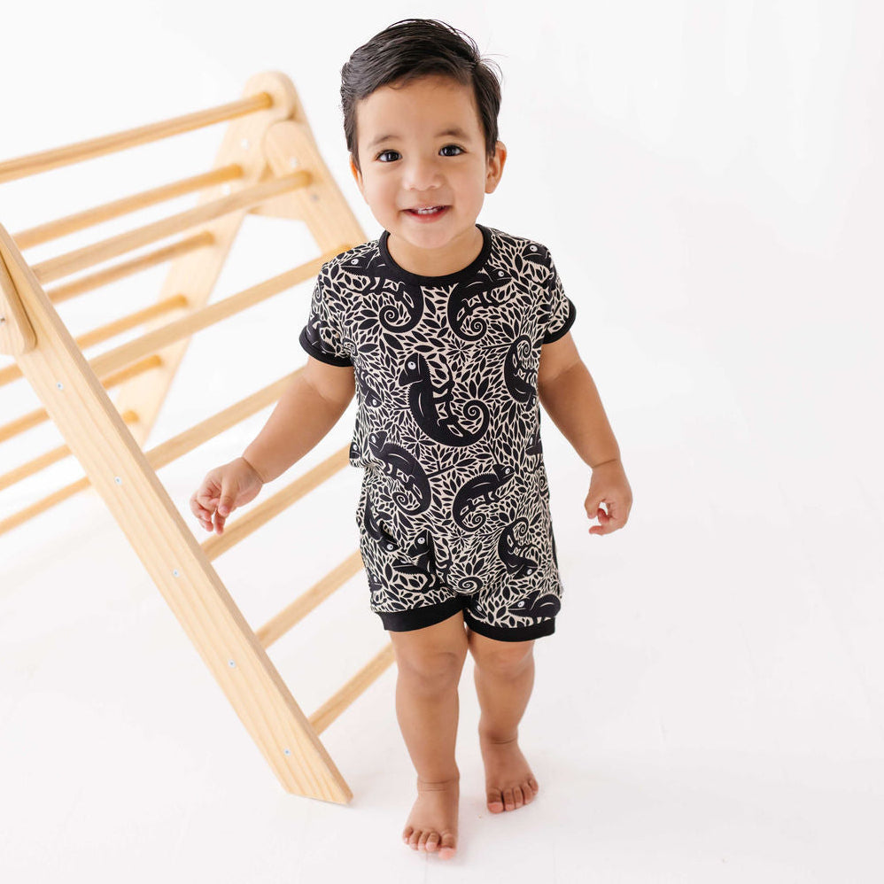 Child wearing a black and white patterned outfit standing next to a wooden climbing toy on a white background