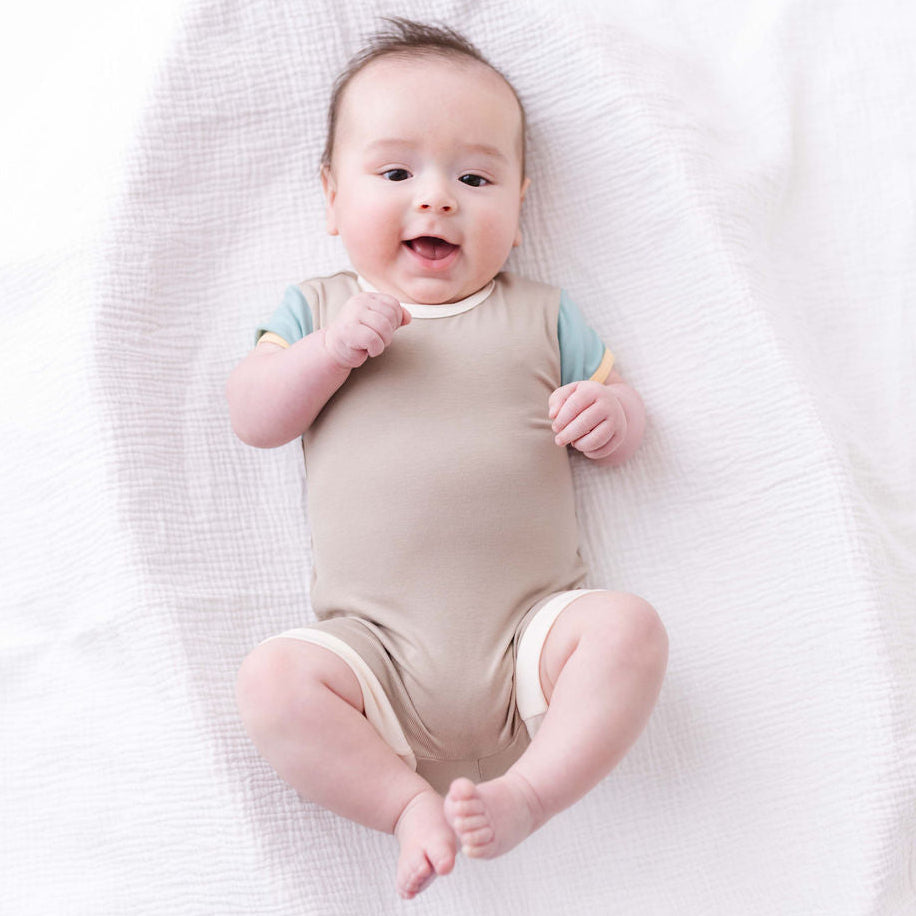 Baby in a beige onesie lying on a white blanket
