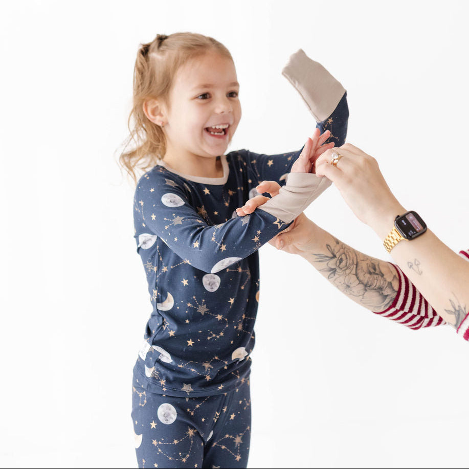 Child wearing a blue nightgown with space-themed print, being helped by an adult on a white background.
