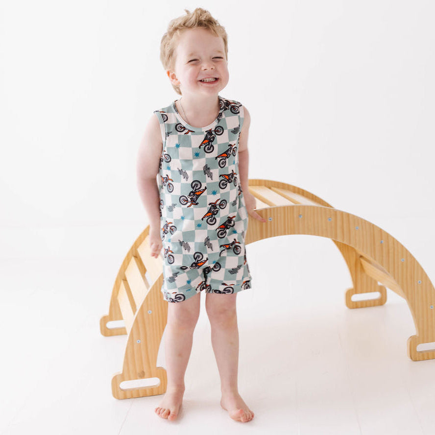 Child wearing a patterned romper standing next to a wooden arch on a white background