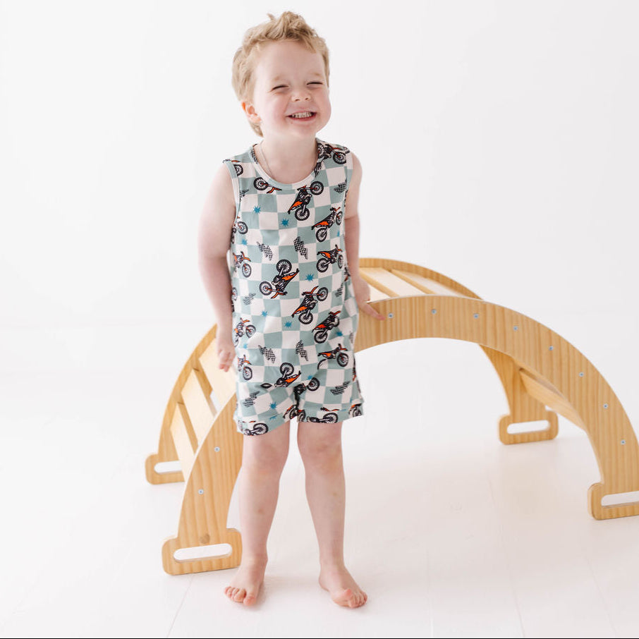 Child wearing a patterned romper standing next to a wooden arch on a white background