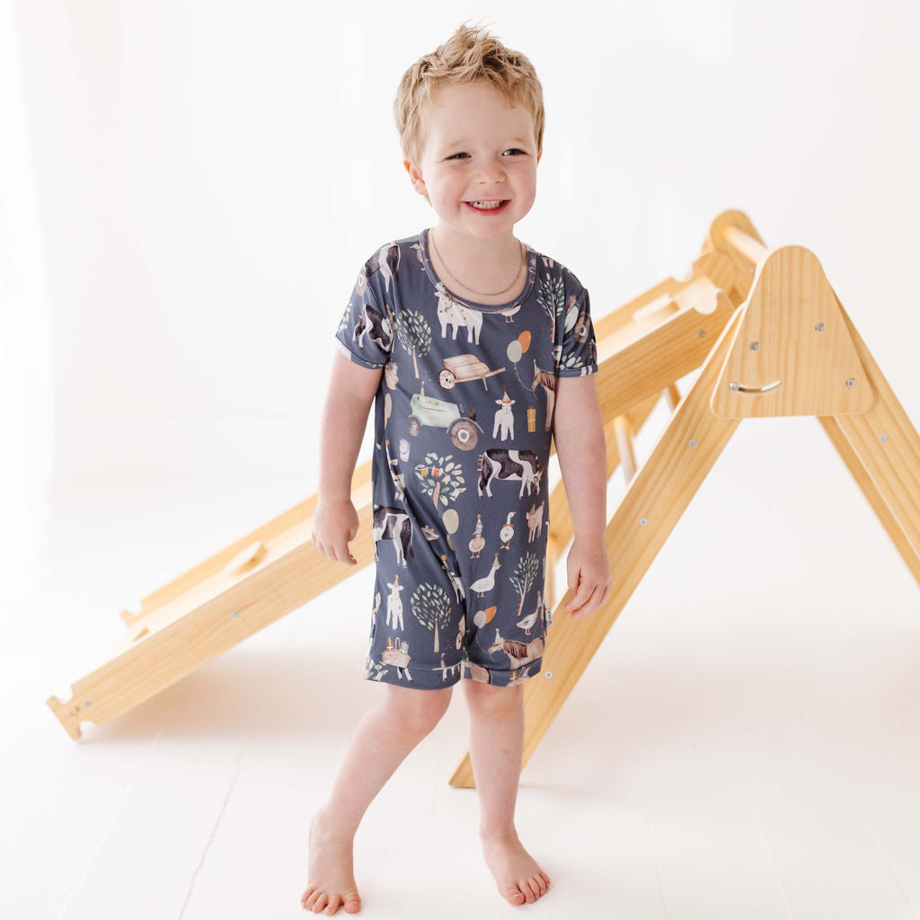 Child wearing a patterned outfit standing in front of a wooden climbing frame on a white background