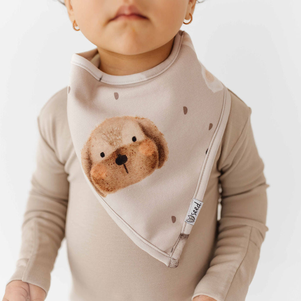 Child wearing a beige long-sleeve shirt with a cartoon otter design on a plain background