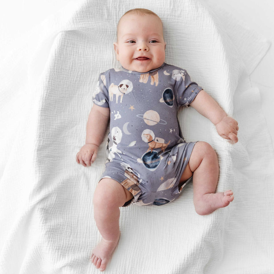Baby wearing a purple onesie with space-themed design on a white blanket