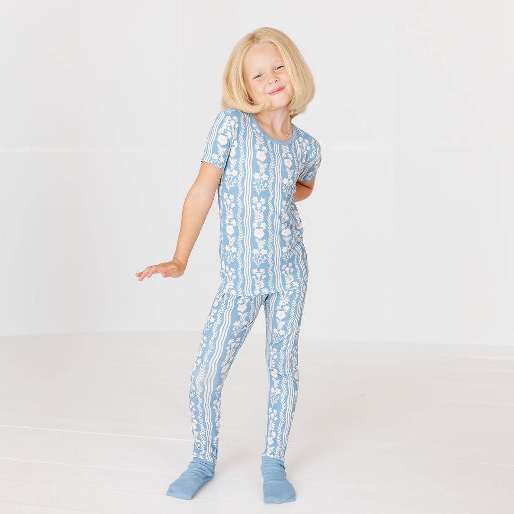 A young blonde girl wearing a light blue and white patterned short-sleeve pajama set with matching socks, posing in a bright white studio.