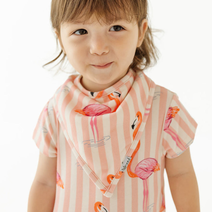 A toddler girl wearing a pink and white striped bib with a flamingo print, photographed against a clean white background.
