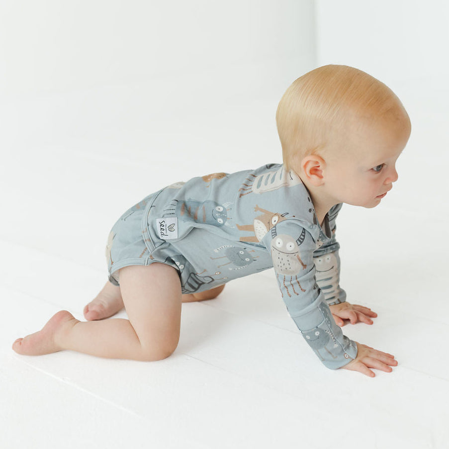 A baby crawling on a white floor wearing a light blue long-sleeve romper with a woodland animal print, including a deer on the chest and owl on the sleeve.