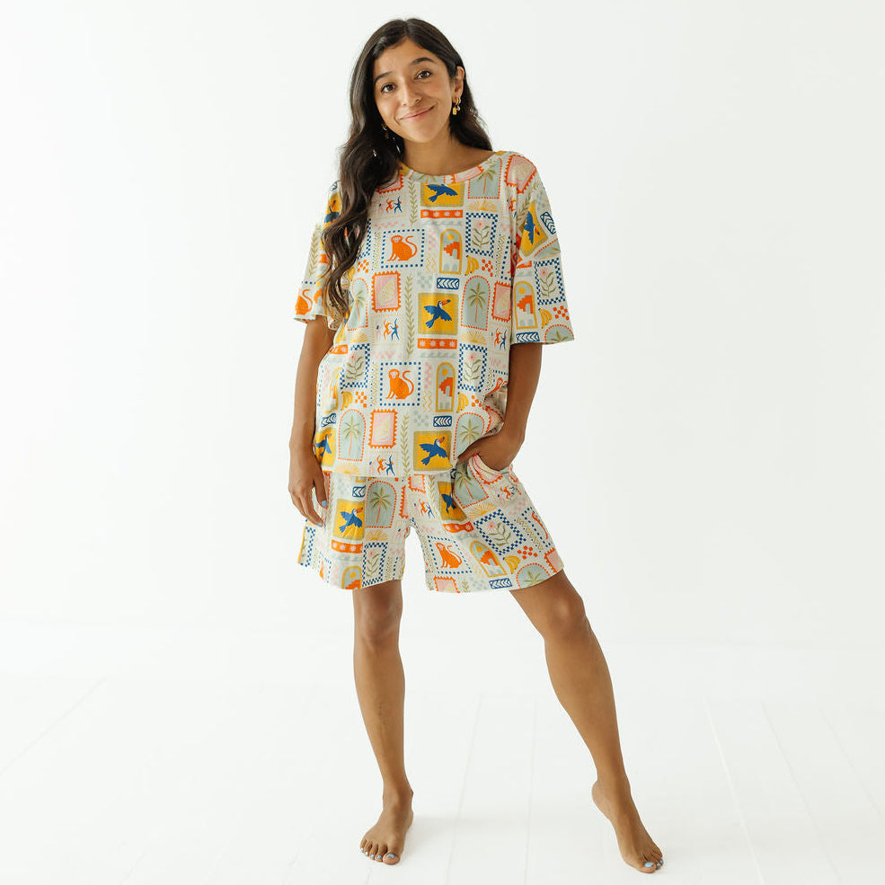 A woman modeling a matching two-piece pajama set with a colorful Egyptian-themed print, consisting of a short-sleeve top and shorts, against a plain white studio background.