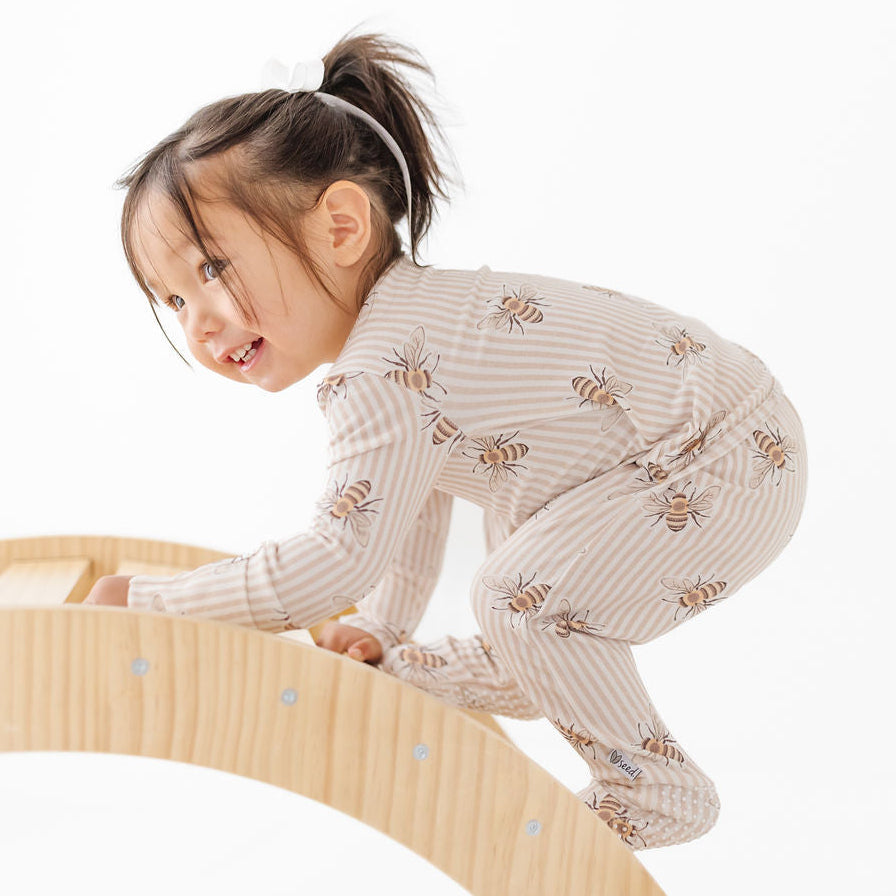 Child in a patterned outfit climbing on a wooden structure against a white background