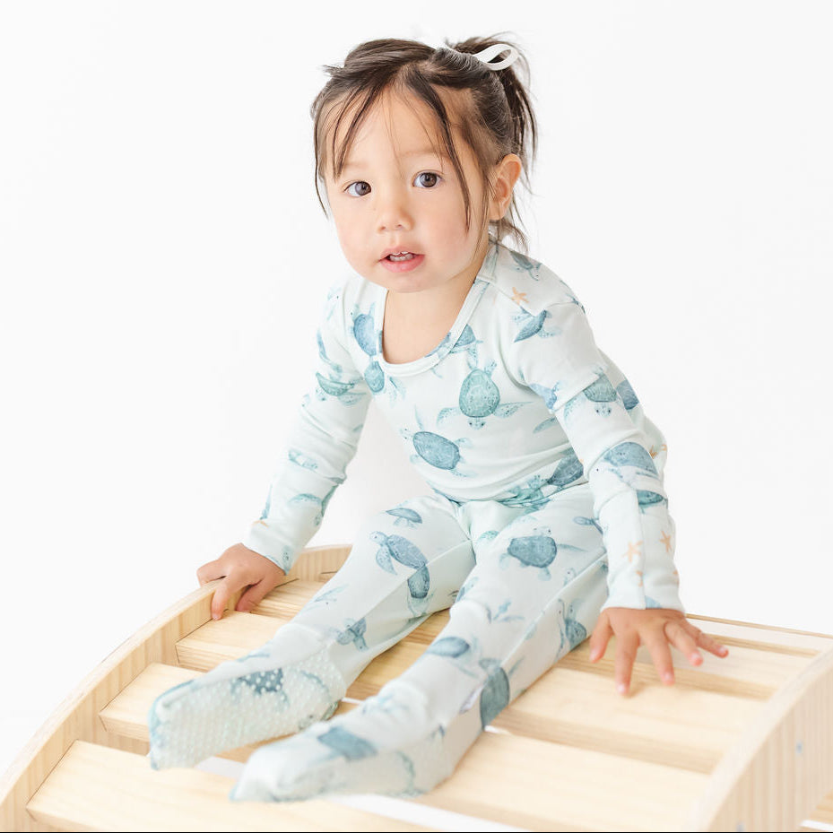 Child wearing a white onesie with blue whale pattern sitting on a wooden surface.