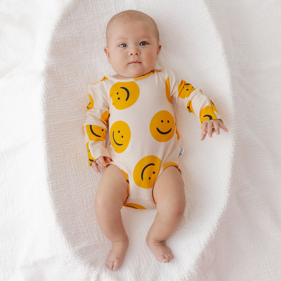 Baby wearing a onesie with smiley face patterns on a white background
