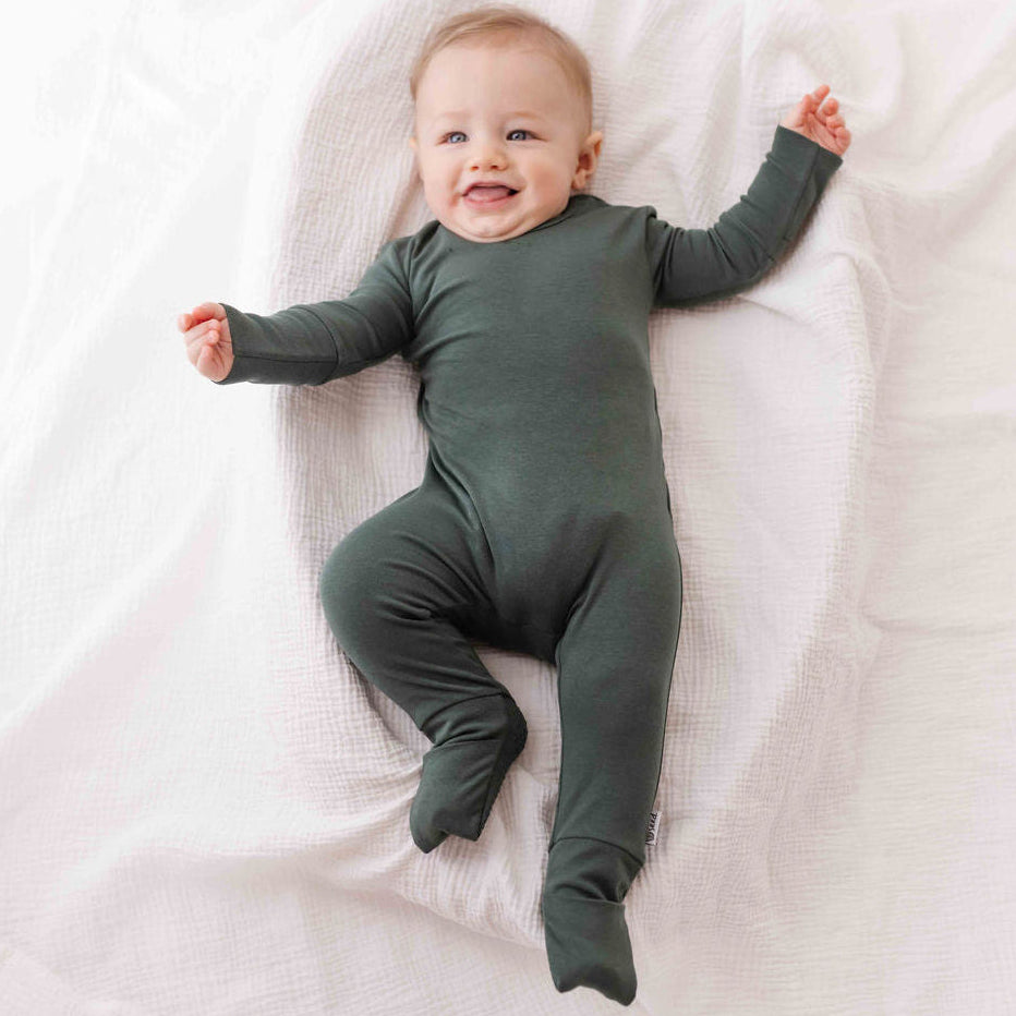 Baby wearing a green onesie lying on a white blanket