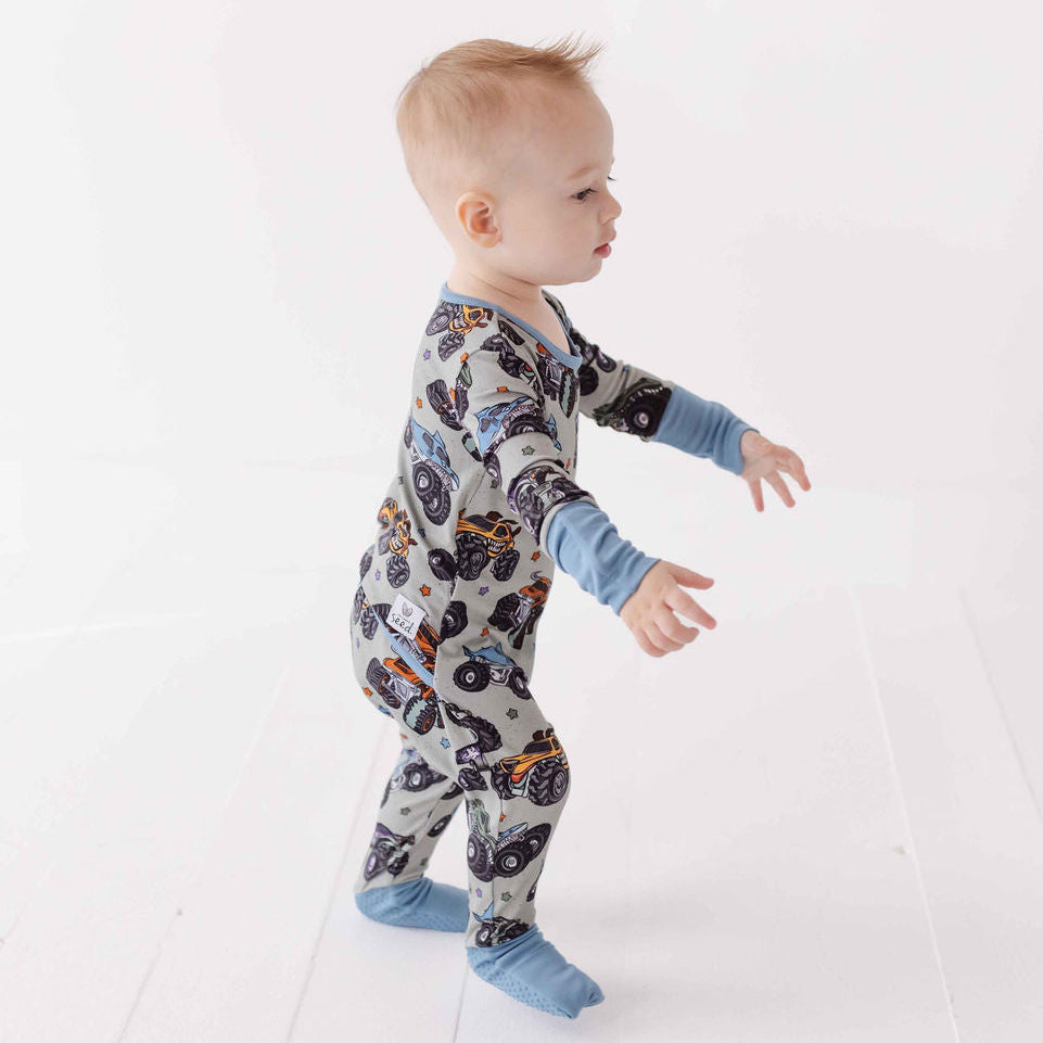 Baby wearing a patterned onesie with long sleeves and blue pants on a white background