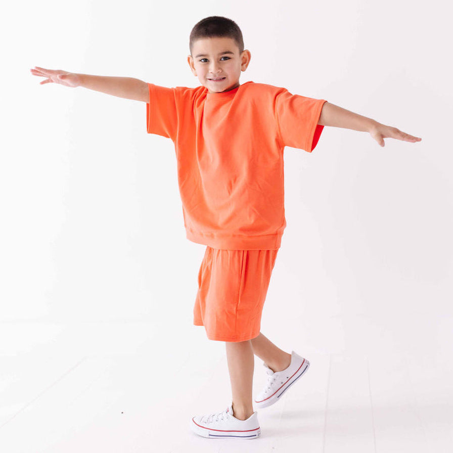 Child wearing an orange outfit with white sneakers on a white background
