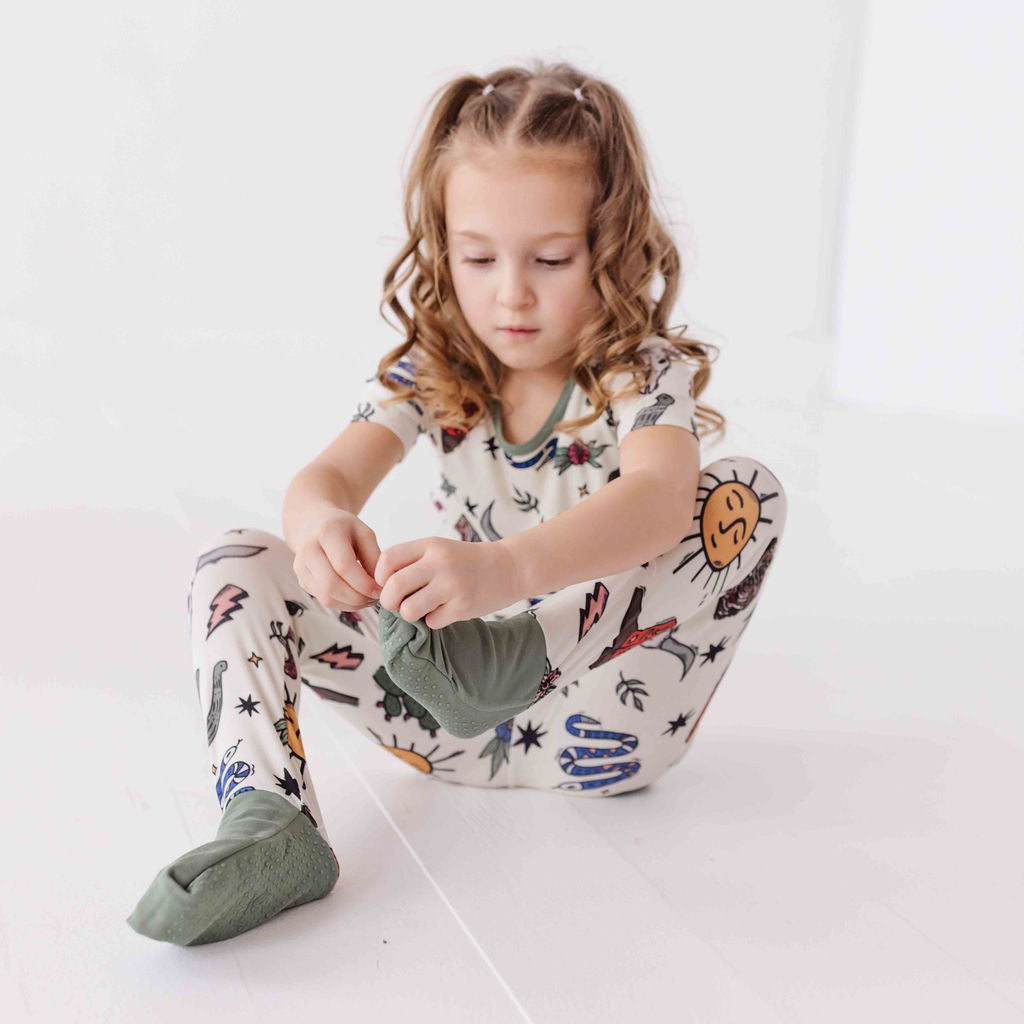Child wearing a patterned onesie sitting on a white floor.