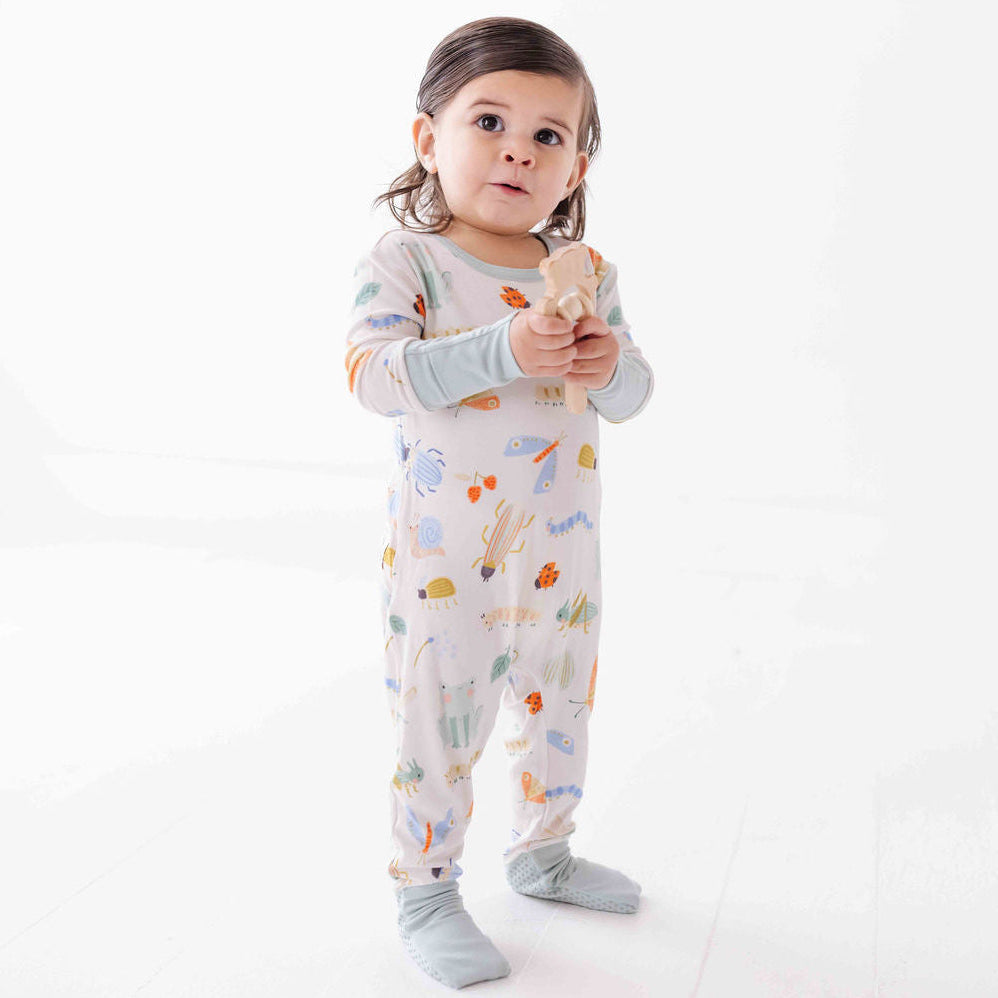 Child wearing a patterned onesie holding a wooden toy on a white background