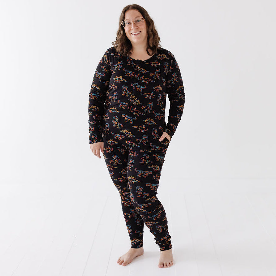 A woman wearing a matching black long-sleeve pajama top and pants set with an all-over orange and blue pattern, standing against a clean white studio background.