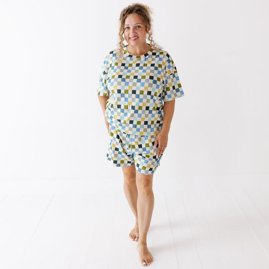 A woman modeling a matching two-piece lounge set consisting of a short-sleeve top and shorts, featuring a geometric checkered pattern in light blue, yellow, and dark green on a white background.