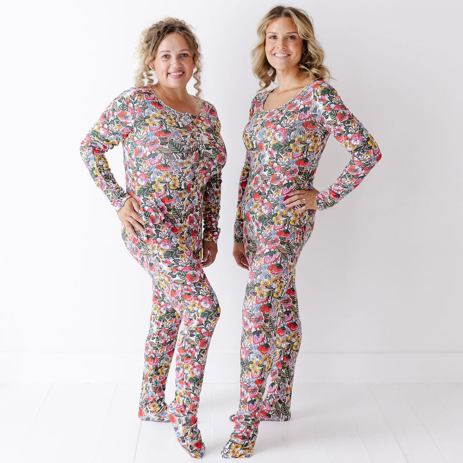 Two women modeling matching long-sleeve jumpsuits with a colorful floral print, standing against a plain white studio background.