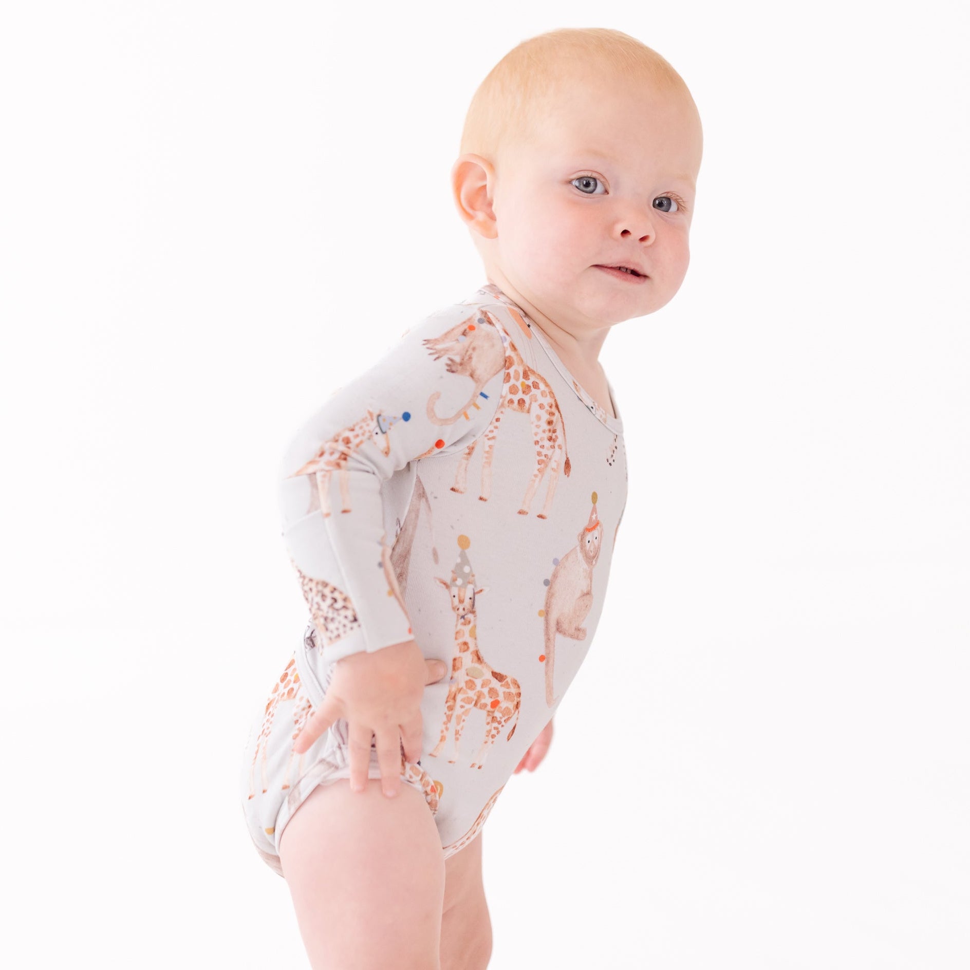 Baby wearing a long-sleeve onesie with giraffe pattern on a white background